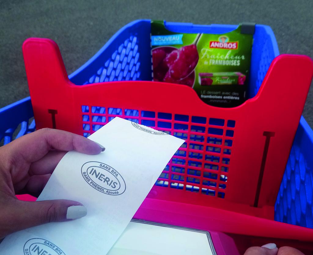 Personne qui tient un ticket de caisse à la main en poussant son chariot de courses.
