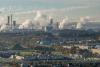 Photo d'une ville avec, en fond, une usine dont les cheminées rejettent des fumées blanches