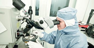 Femme en tenue de protection qui observe au microscope des nanomatériaux